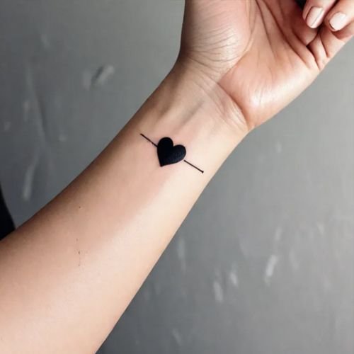 piccolo tatuaggio a forma di cuore nero sul polso di una donna, che simboleggia amore ed eleganza